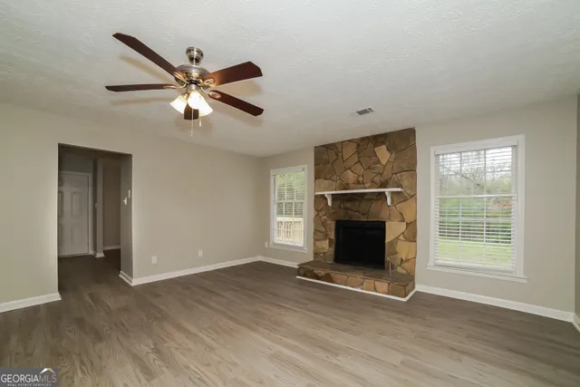 a view of an empty room with wooden floor fireplace and a window