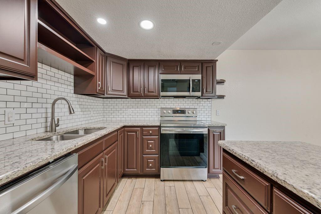219 West Rochelle Road Irving, TX 75062 - Photo 11 of 29 Kitchen featuring wood-finish cabinetry, granite countertops, subway tile backsplash, and stainless steel appliances