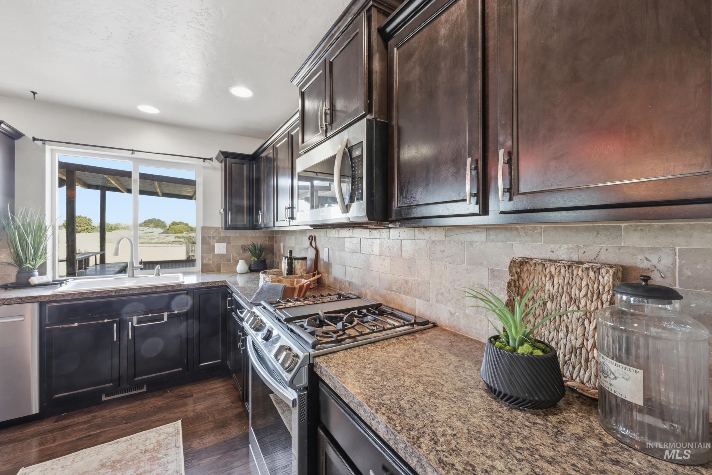 4855 South Chex Way Boise, ID 83709 - Photo 16 of 47 Kitchen featuring dark wood cabinetry, a gas range with a built-in microwave, stone-look countertops, and a tiled backsplash