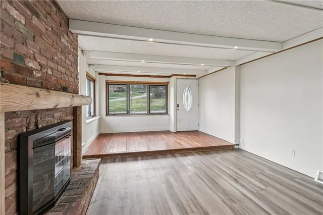 a view of an empty room with wooden floor fireplace and a window