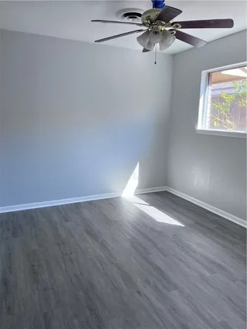 an empty room with wooden floor fan and windows