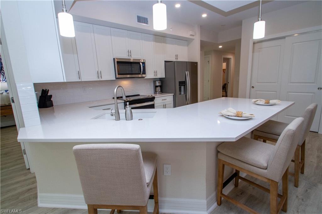268 Indies Drive East, Unit 102 Naples, FL 34114 - Photo 10 of 48 a kitchen with stainless steel appliances a white table chairs and a refrigerator