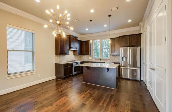 a kitchen with stainless steel appliances granite countertop a refrigerator a sink dishwasher a stove and a dining table with wooden floor