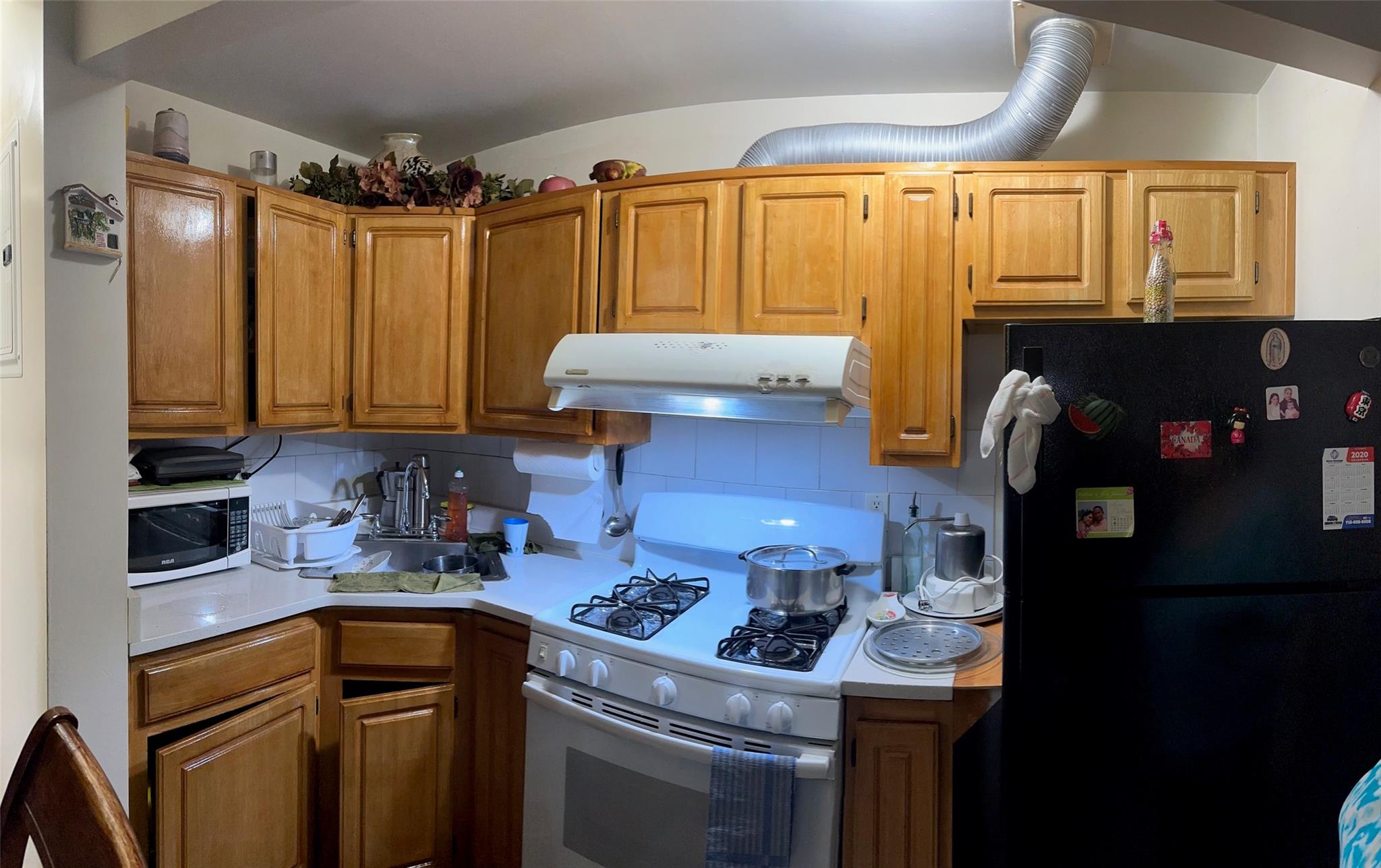 106-19 50th Avenue, Unit 2F Queens, NY 11368 - Photo 2 of 8 Kitchen featuring white appliances, under cabinet range hood, light countertops, tasteful backsplash, and brown cabinets