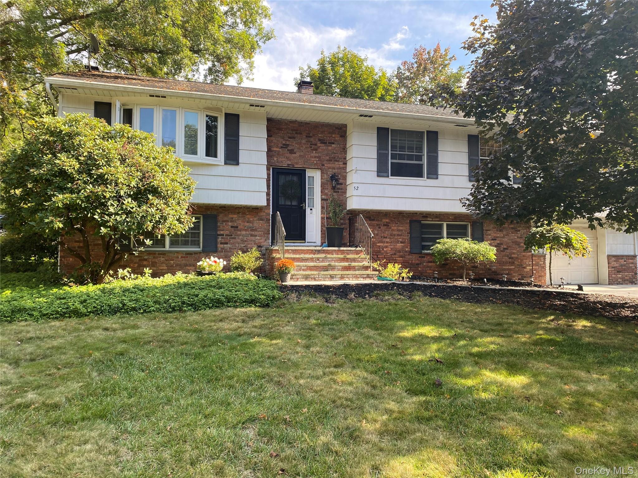 Bi-level home with brick siding, a front yard, a chimney, and a garage