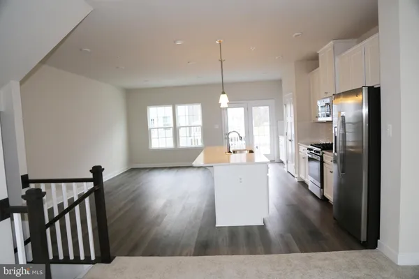 a living room with stainless steel appliances furniture wooden floor and a view of kitchen