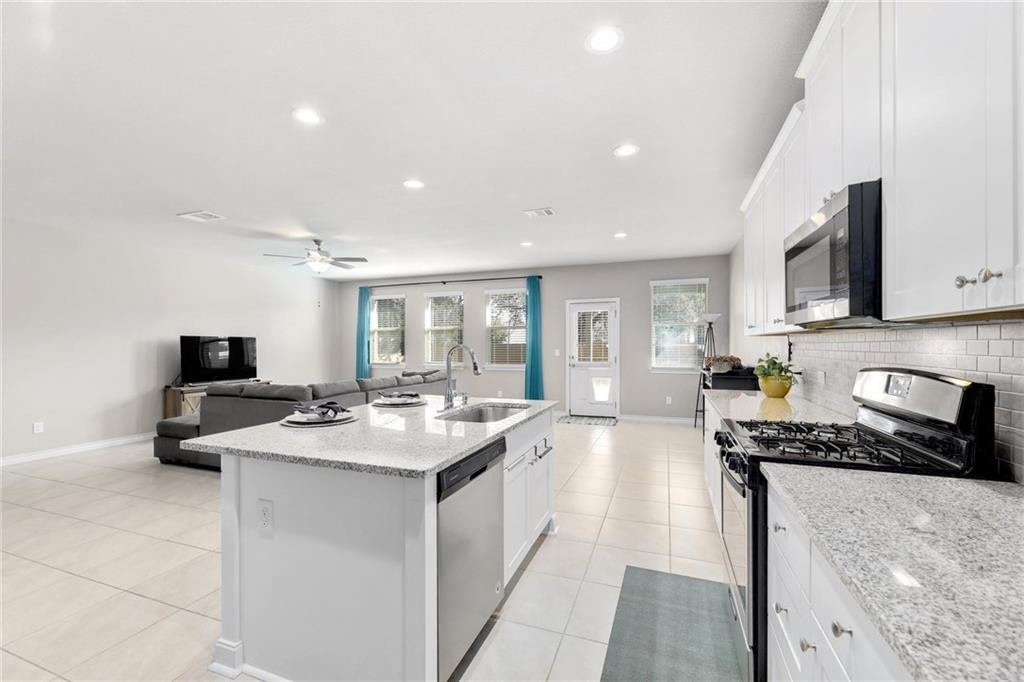 204 Tulum Terrace Leander, TX 78641 - Photo 20 of 22 Kitchen featuring stainless steel appliances, white cabinets, light stone countertops, open floor plan, and light tile patterned floors