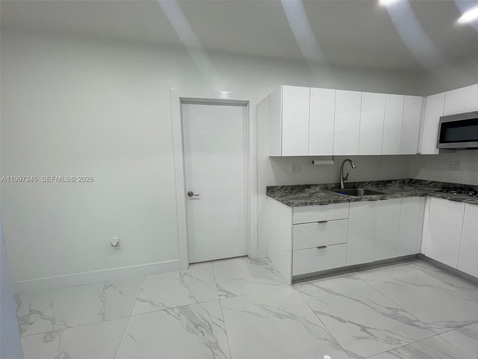 15426 Southwest 168th Terrace, Unit 2 Miami, FL 33187 - Photo 8 of 12 a kitchen with granite countertop white cabinets and white appliances