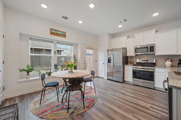 a kitchen with stainless steel appliances kitchen island granite countertop a stove a refrigerator a sink a dining table and chairs with wooden floor