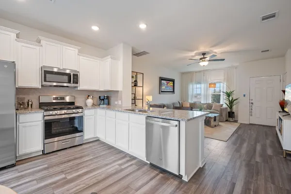 a kitchen with stainless steel appliances a stove top oven a sink dishwasher a refrigerator and white cabinets with wooden floor