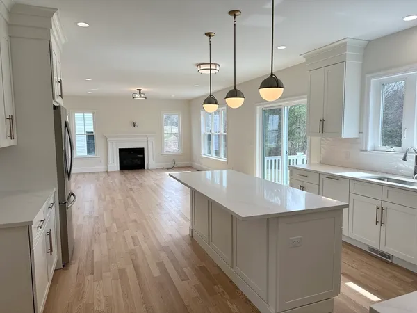 a large kitchen with stainless steel appliances a large center island wooden floor sink and a window