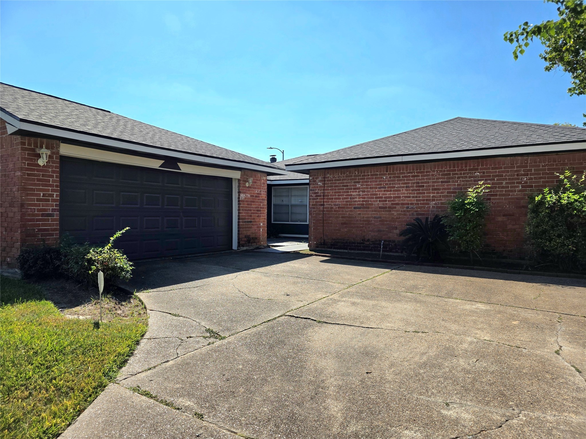 1323 Padstow Lane Channelview, TX 77530 - Photo 2 of 11 This photo shows a single-story brick home with a two-car garage and a spacious driveway. The exterior features a well-maintained lawn and some shrubs, creating a neat and welcoming appearance.