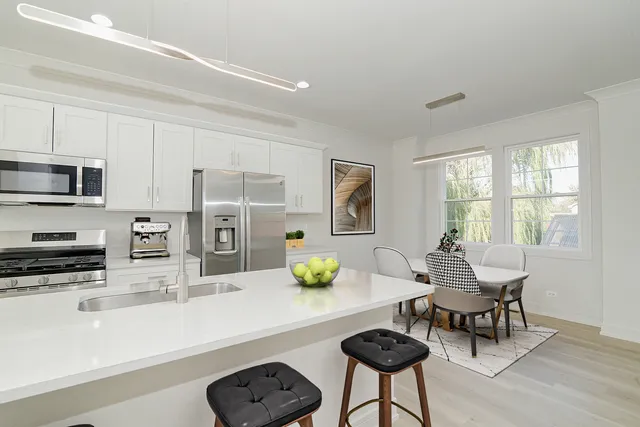 a kitchen with stainless steel appliances granite countertop a stove a sink a microwave a dining table and chairs with white cabinets