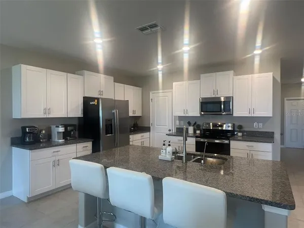 a kitchen with stainless steel appliances kitchen island granite countertop a stove a sink a refrigerator a dining table and chairs with wooden floor