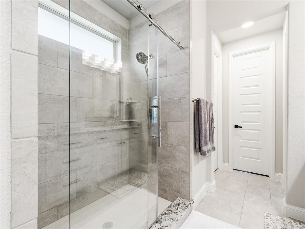 15340 Crape Myrtle Road Frisco, TX 75035 - Photo 23 of 40 Glass-enclosed shower with a chrome showerhead, light gray tile surround, and a coordinating granite curb