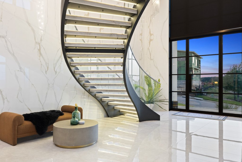A grand entrance welcomes you with a floating spiral staircase, gleaming tile floors, and a dramatic wall of windows.