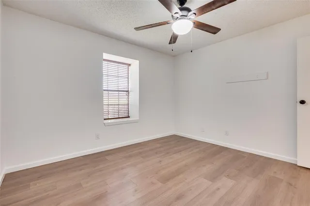 an empty room with wooden floor fan and windows