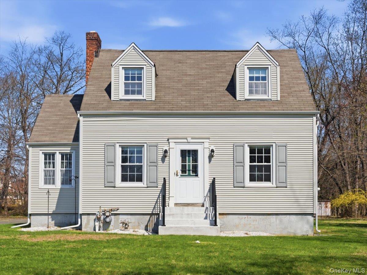 Charming property featuring a light-colored exterior with grey shutters, a grey roof, and a prominent red brick chimney