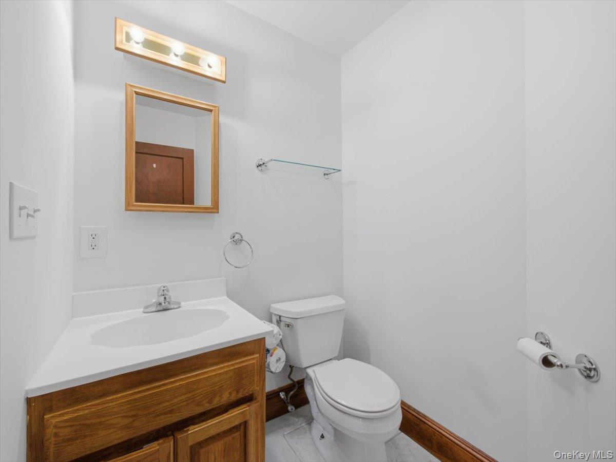 311 Gate Hill Coop Road Stony Point, NY 10980 - Photo 20 of 42 The bathroom features a wooden vanity with a white countertop and an integrated sink, a wall-mounted mirror with a wooden frame, and a toilet