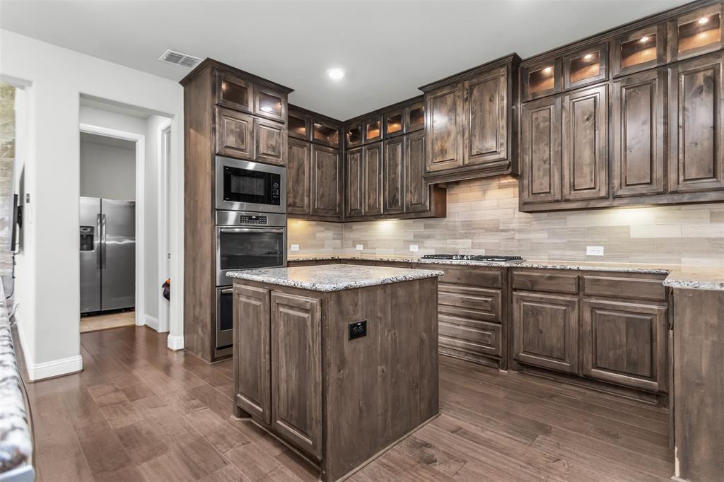 6333 Hall Road Frisco, TX 75034 - Photo 18 of 38 Spacious kitchen featuring rich wood cabinetry, stainless steel double ovens, and a central island with a granite-style countertop