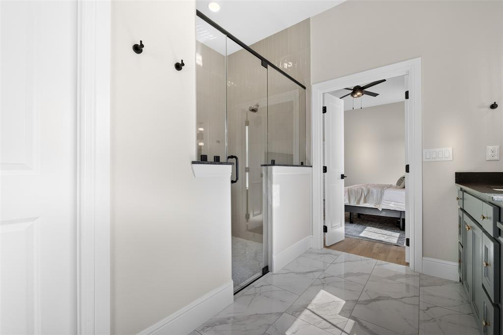 10978 Gregory Road Sanger, TX 76266 - Photo 25 of 40 Glass-enclosed shower with matte black hardware, tiled shower surround, marble-finish floor tiles, and a built-in vanity with dark countertop