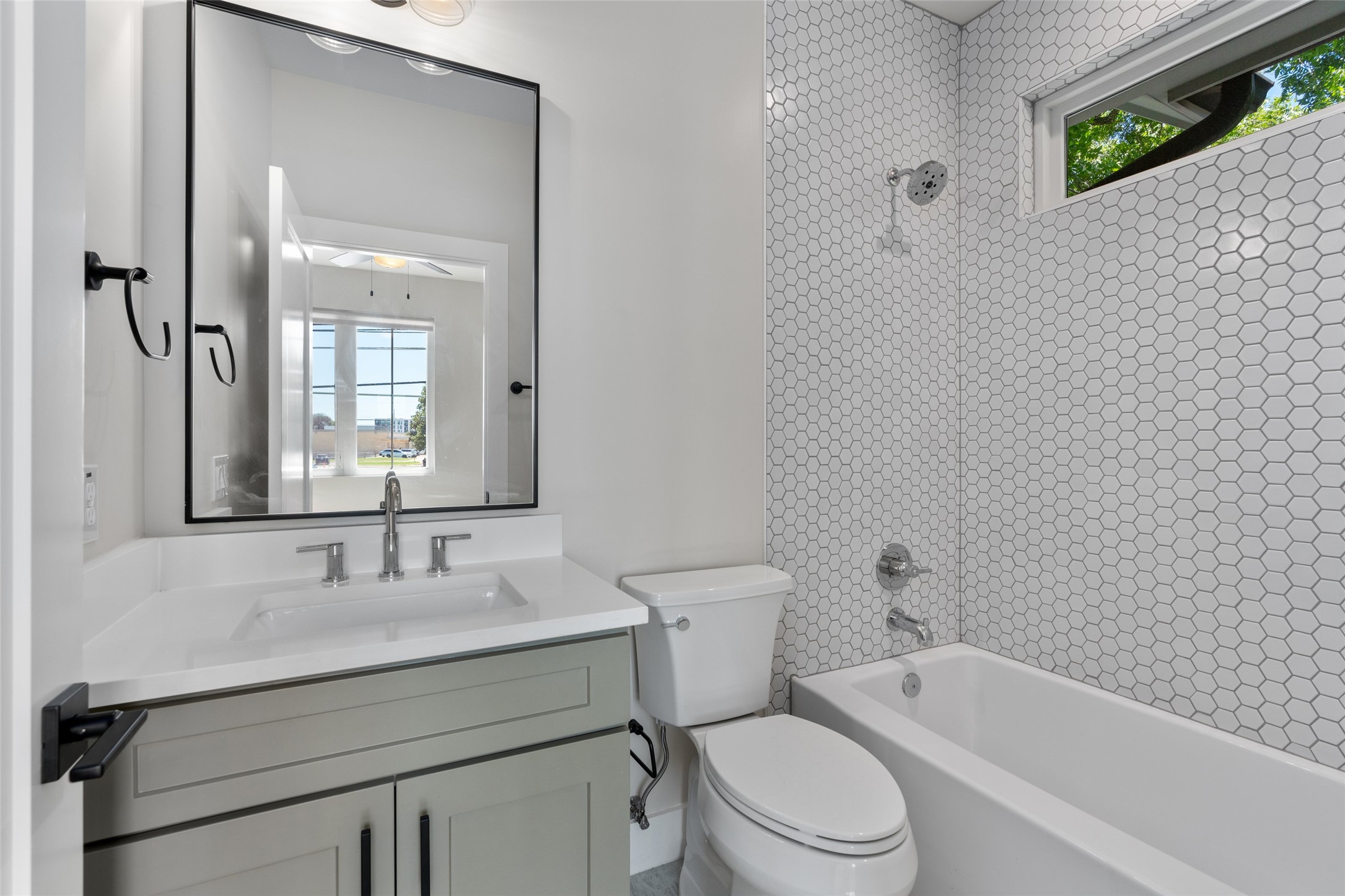 5200 Grover Avenue Austin, TX 78756 - Photo 24 of 32 Full bathroom in the secondary bedroom. Featuring white quartz countertops, a white bathtub with a chrome showerhead, white hexagonal wall tiling, and a window