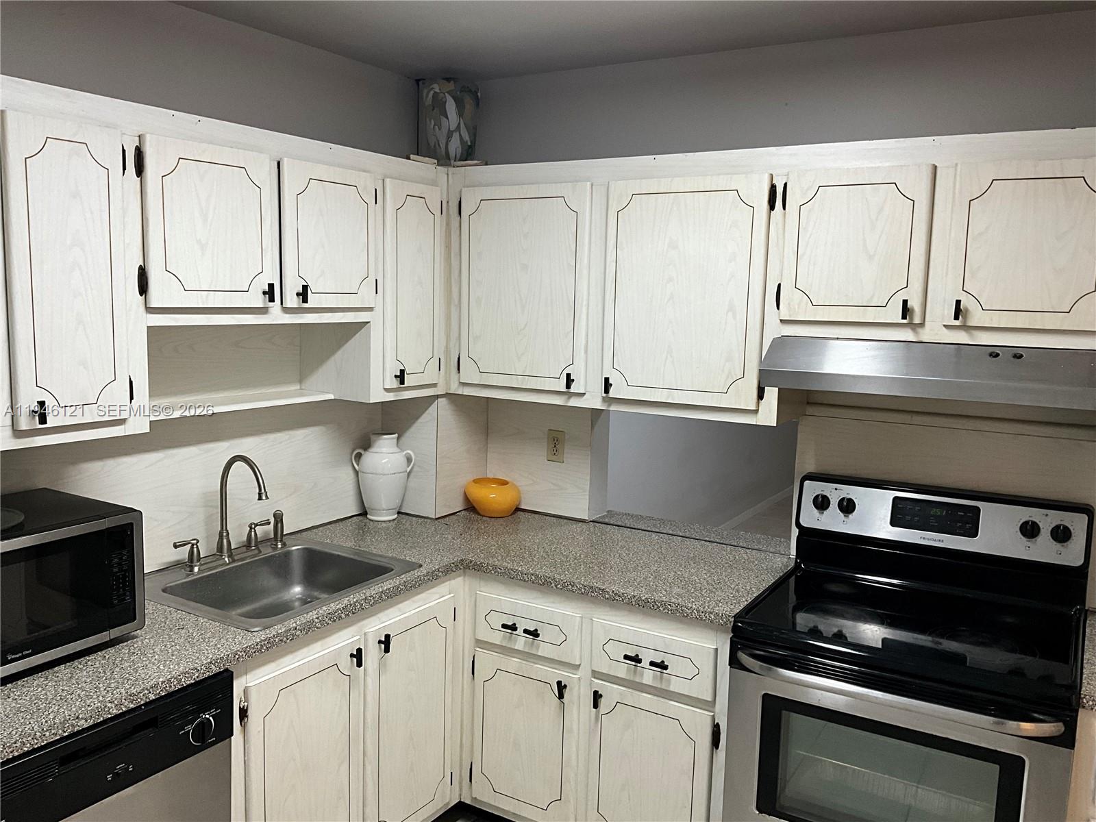 101 Berkley Road, Unit 205 Hollywood, FL 33024 - Photo 11 of 13 a kitchen with granite countertop white cabinets and black appliances