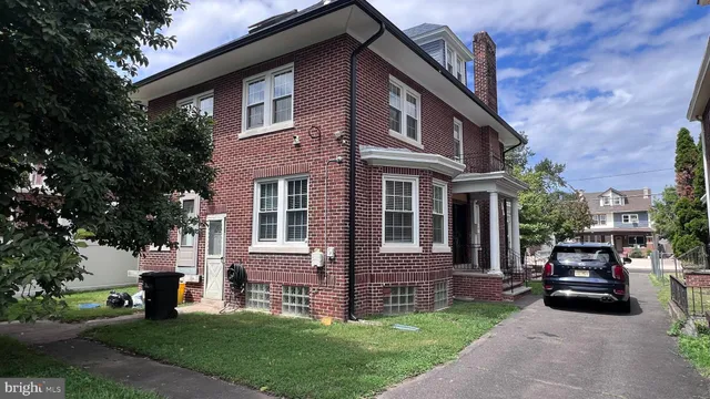 a view of brick house with a yard plants and large tree