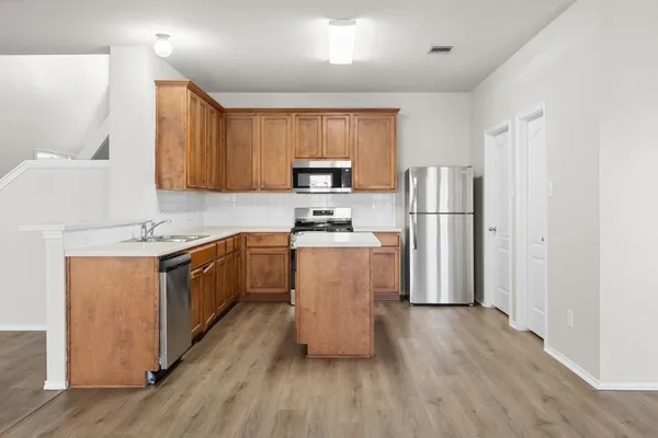 a kitchen with a refrigerator a stove top oven a sink and cabinets with wooden floor