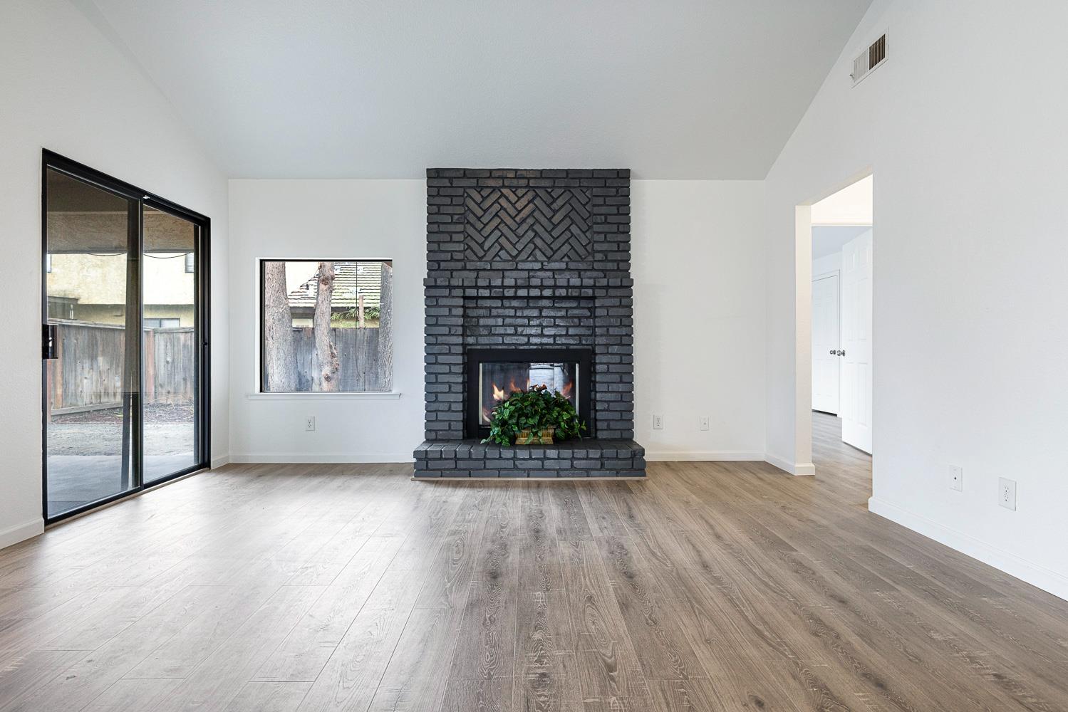 929 Barnett Way Madera, CA 93637 - Photo 4 of 23 an empty room with wooden floor fireplace and windows