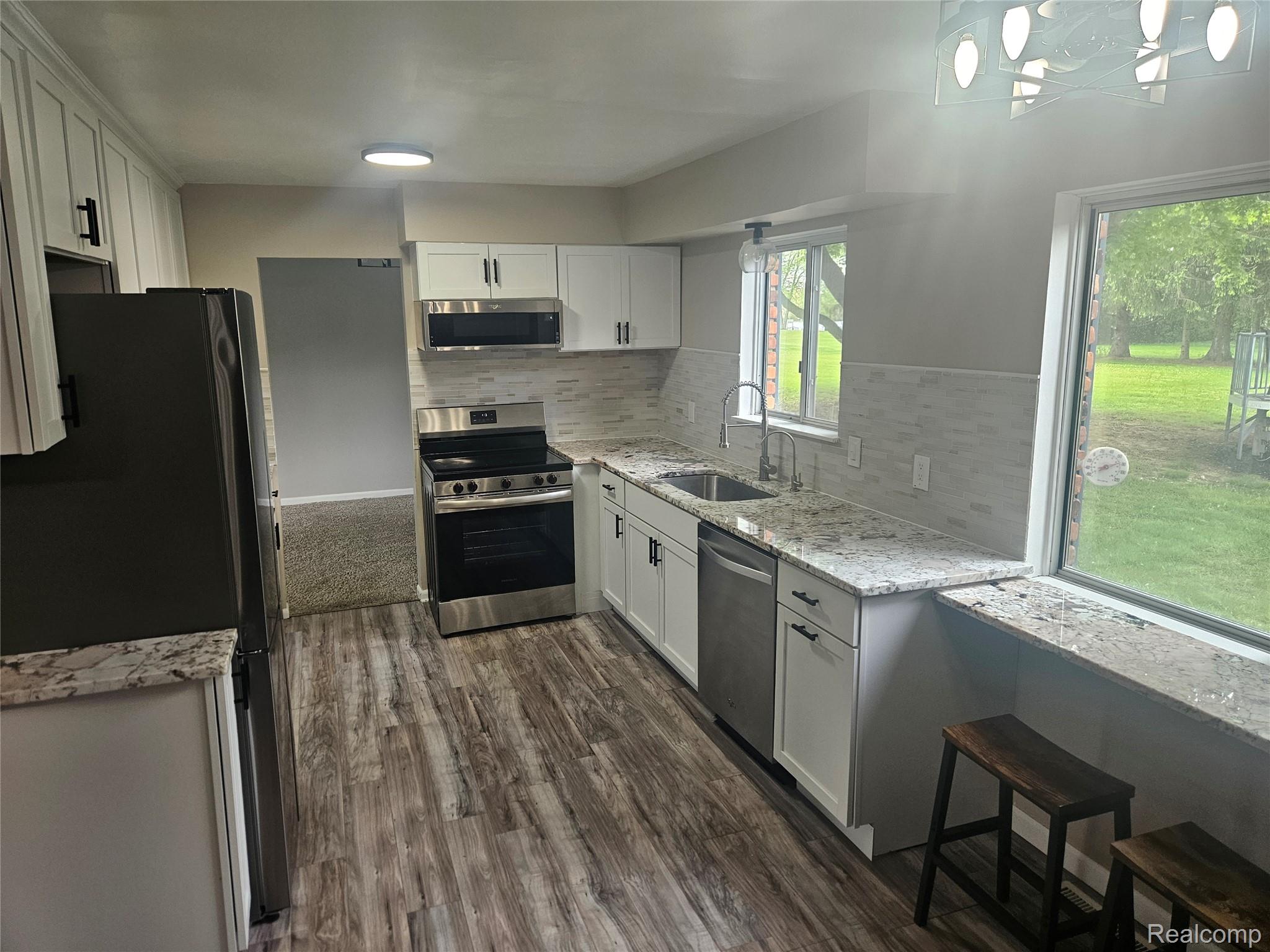 1210 Bay Ridge Drive Highland, MI 48356 - Photo 4 of 25 Kitchen featuring white cabinets, stainless steel appliances, light stone countertops, and tasteful backsplash