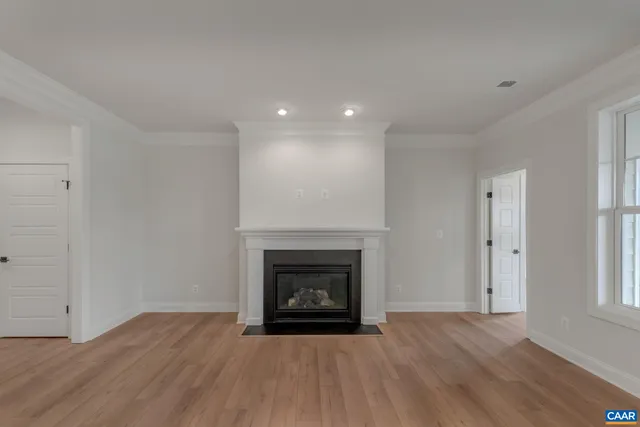 a view of an empty room with wooden floor fireplace and a window