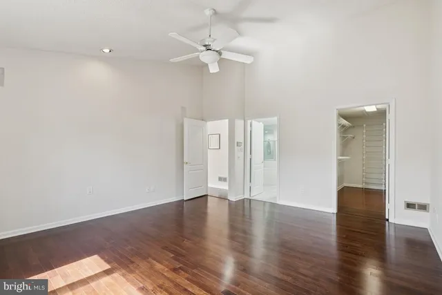 a view of an empty room with wooden floor and a ceiling fan