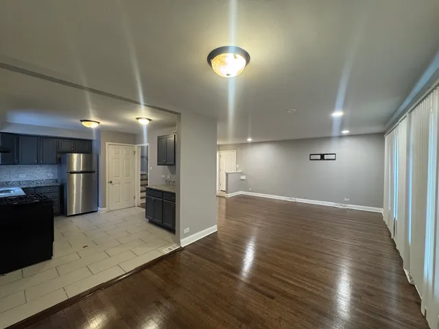 an empty room with wooden floor kitchen view and a window