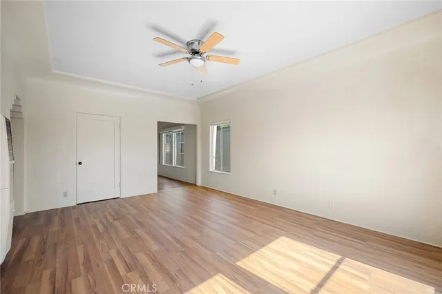 an empty room with wooden floor chandelier fan and windows