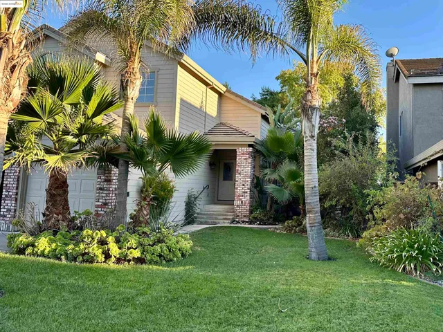 a view of an empty room and kitchen with a large window wooden floor and a ceiling fan