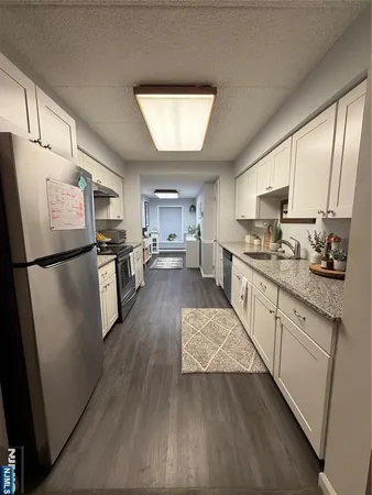 a kitchen with stainless steel appliances granite countertop a refrigerator a stove a sink dishwasher and white cabinets with wooden floor