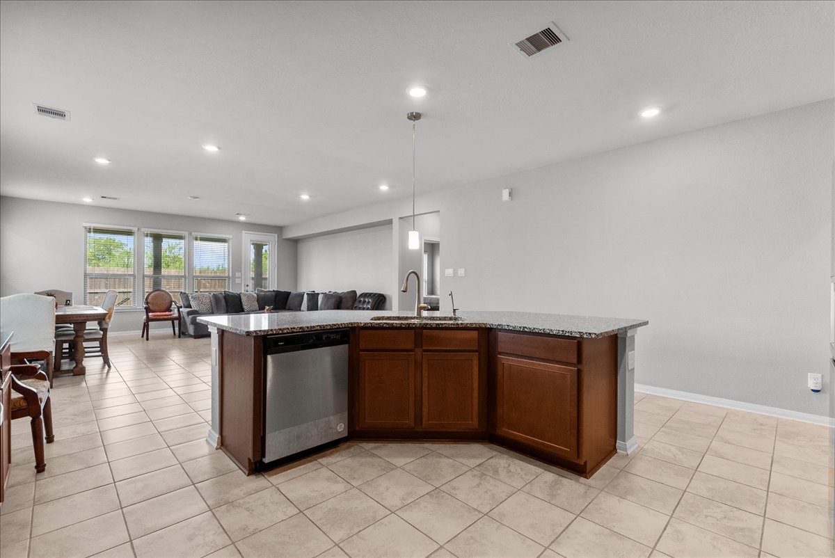 2320 Rosemary Street Rosenberg, TX 77469 - Photo 12 of 40 Bright, open-concept living space with a modern kitchen featuring granite countertops and a central island. The room has tiled flooring, recessed lighting, and large windows for natural light, offering a seamless flow to the dining and living areas.