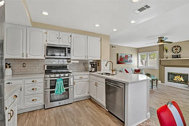 a kitchen with stainless steel appliances granite countertop a stove top oven a sink dishwasher and white cabinets with wooden floor