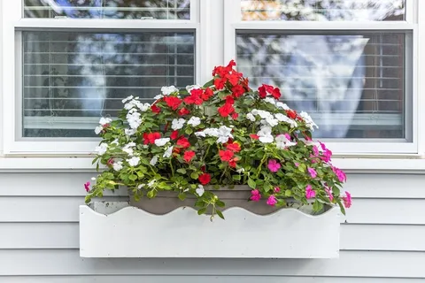 a flower vase with flowers sitting in front of a window