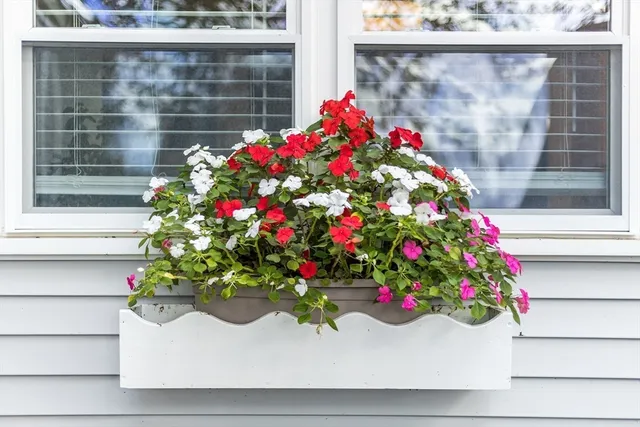 a flower vase with flowers sitting in front of a window