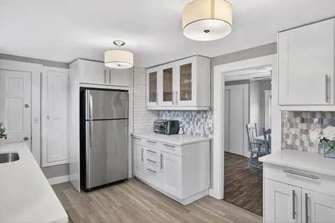 a kitchen with stainless steel appliances granite countertop a refrigerator a stove a sink and white cabinets with wooden floor