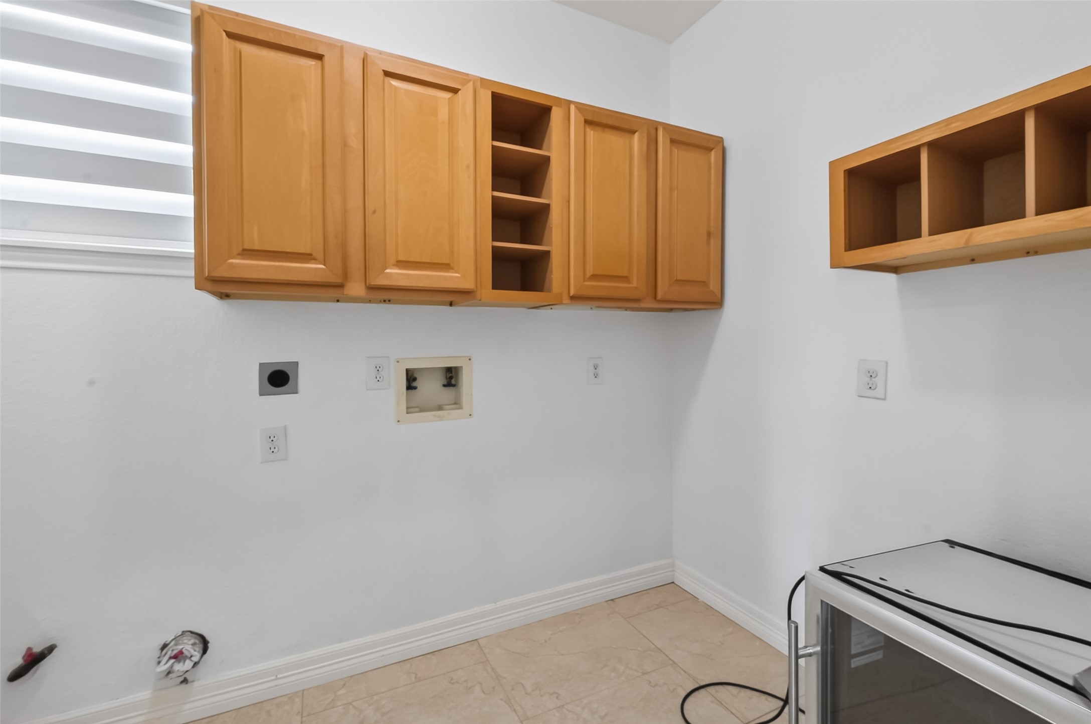 1311 Rene Court Sugar Land, TX 77479 - Photo 17 of 45 This photo shows a laundry room with light wooden cabinets, hookups for a washer and dryer, and tiled flooring. The space is well-lit with a window providing natural light.