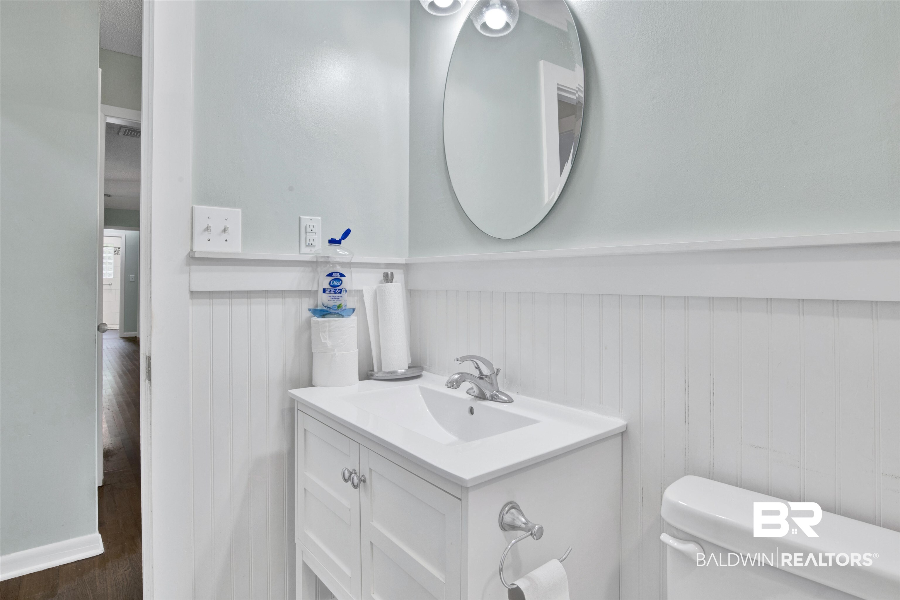 17714 Horseneck Road Bay Minette, AL 36507 - Photo 5 of 36 Bathroom featuring a white vanity with integrated sink, chrome faucet, oval wall-mounted mirror, two-light fixture, beadboard wainscoting, and a white toilet