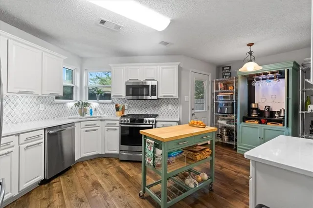 a kitchen with stainless steel appliances granite countertop a stove top oven a sink dishwasher a dining table and chairs with wooden floor