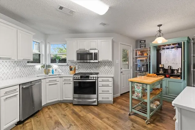 a kitchen with stainless steel appliances granite countertop a stove top oven a sink dishwasher a dining table and chairs with wooden floor