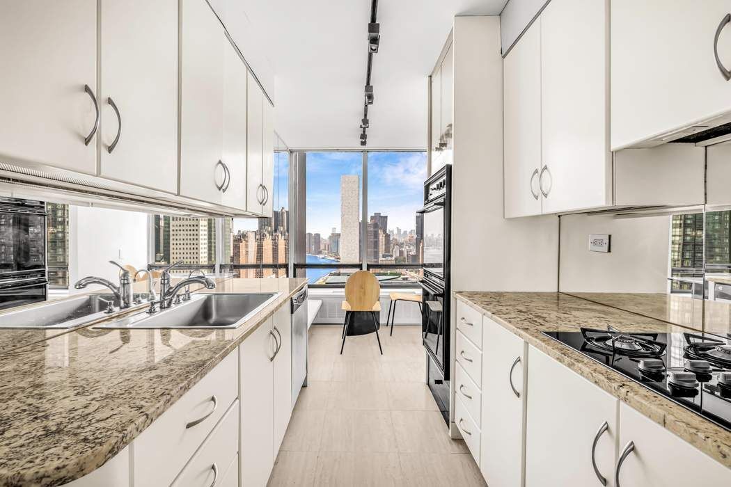 870 United Nations Plaza, Unit 28A Manhattan, NY 10017 - Photo 7 of 28 a kitchen with stainless steel appliances granite countertop a sink a stove and a wooden cabinets
