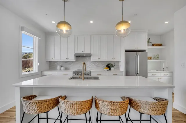 a kitchen with stainless steel appliances granite countertop a sink a stove a refrigerator and white cabinets with wooden floor