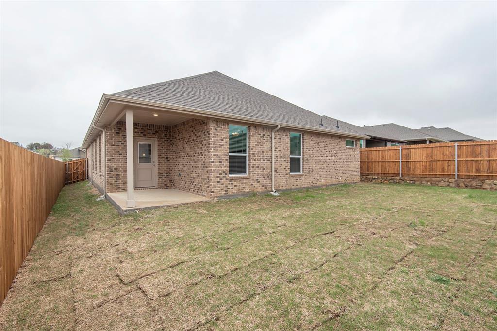 2301 Ruff Road Denton, TX 76205 - Photo 22 of 23 Rear exterior with brick facade, covered patio, private fenced yard, multiple windows, and a dark shingle roof