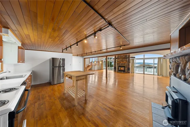 a view of an empty room with wooden floor and a kitchen